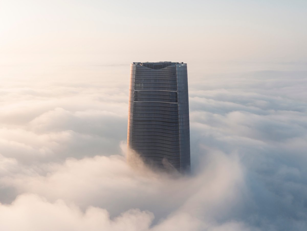 A futuristic skyscraper rising above a sea of clouds at sunrise, representing digital growth and ambition